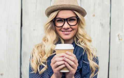 Sobre programas de fidelización Chica joven y moderna con sombrero y gafas sostiene en sus manos un vaso de café de papel del estilo Starbucsks