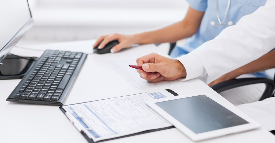 Big data sanitario, una enfermera y un doctor revisan gráficas en el ordenador junto a una tablet y una gráfica en papel